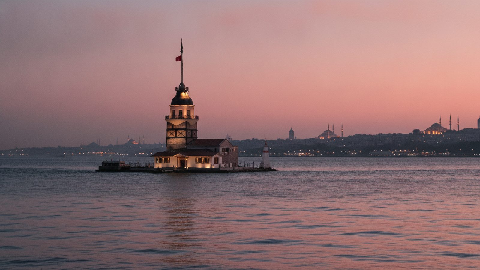 Maiden's Tower (Kız Kulesi) on its islet at the mouth of the Bosphorus at dusk, lighthouse glowing against the Istanbul skyline